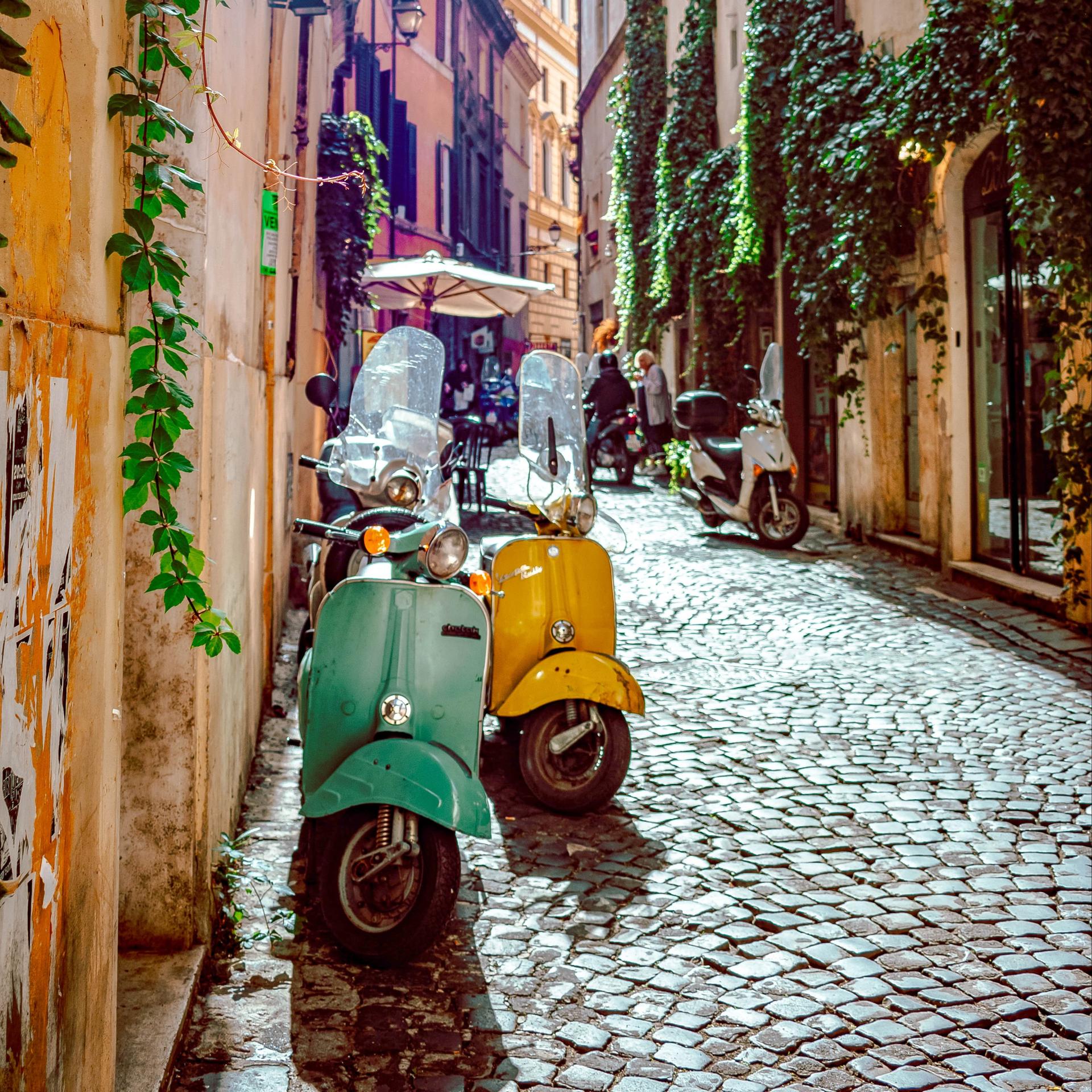 A pair of vespas parked on a street in Italy